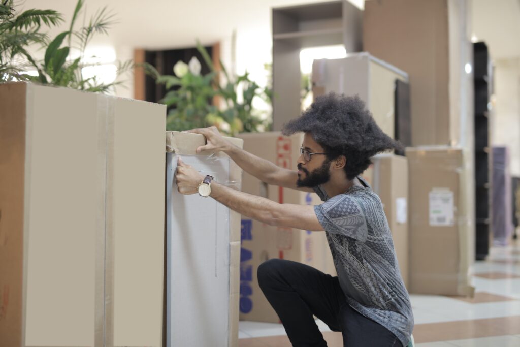 Side view of ethnic bearded man wearing casual clothes and glasses standing in modern office with boxes while preparing for sending