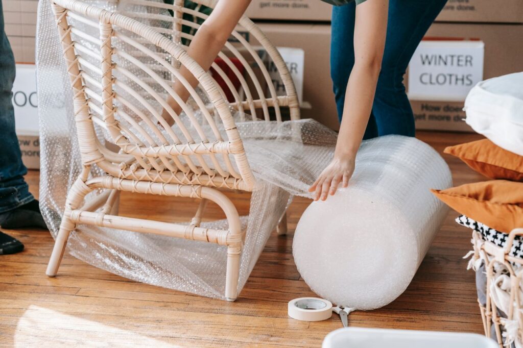 Person wrapping wooden chair with bubble wrap while preparing to move out.
